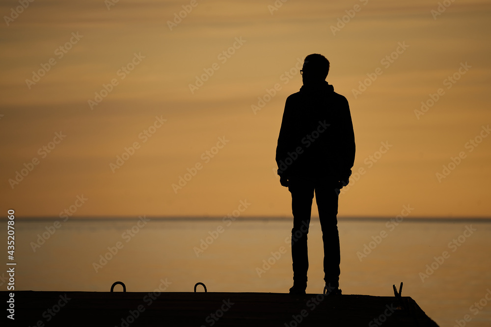 Sticker man standing on rock looking straight. Nature and beauty concept. Orange sundown. Girl silhouette at sunset.