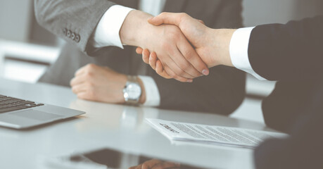 Unknown businessman shaking hands with his colleague or partner above the glass desk in modern office, close-up. Business people group at meeting