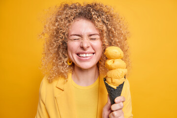 Joyful positive curly haired woman closes eyes from happiness smiles broadly holds tasty appetizing...
