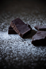 A close up of dark chocolate squares with sugar on a dark wooden table.