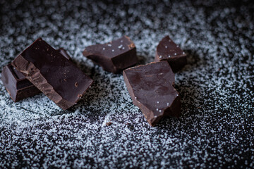 A close up of dark chocolate squares with sugar on a dark wooden table.