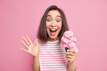 Emotional brunette woman exlaims loudly keeps palm raised eats delicious ice cream reacts on...