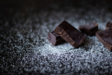 A close up of dark chocolate squares with sugar on a dark wooden table.