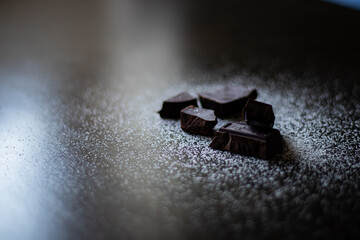 A close up of dark chocolate squares with sugar on a dark wooden table.