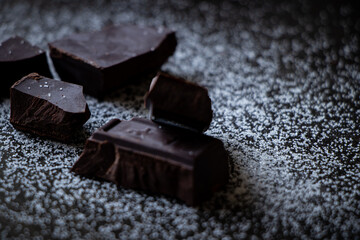 A close up of dark chocolate squares with sugar on a dark wooden table.