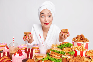 Surprised cheerful Asian woman focused at camera consumes too much fast food suffers calorie...