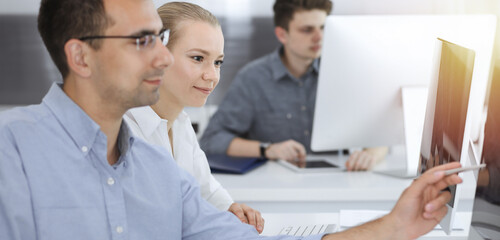 Business people working together in modern office. Happy smiling adult businessman using pc computer with colleagues. Teamwork and partnership concept