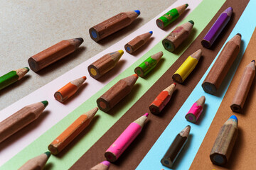Miniature pencils of different colors, a background of lying pencils and paper for drawing pastel.