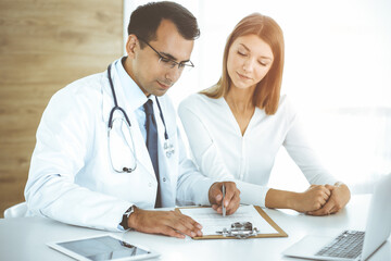 Doctor and patient discussing medical exam results while sitting at the desk in sunny clinic