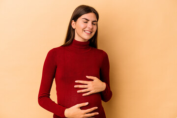 Obraz premium Young caucasian pregnant woman isolated on beige background touches tummy, smiles gently, eating and satisfaction concept.