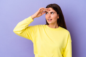 Young caucasian woman isolated on purple background looking far away keeping hand on forehead.