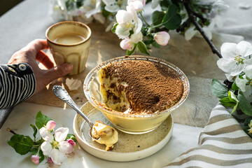 Portion of classic tiramisu in glass bowl, spoon and cup of espresso coffee on wooden board.