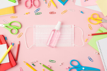 Top view photo of multicolor stationery scissors pens pencils pushpins clips calculator copybooks and sanitizer bottle on medical facemask in the middle isolated pastel pink background