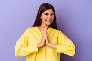 Young caucasian woman isolated on purple background holding hands in pray near mouth, feels confident.