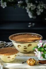 Two glass bowls with classic tiramisu dessert on wooden board on dark blue background.