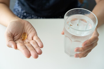 Beautiful young Asian woman holding a fish oil capsule on her hand close up. 