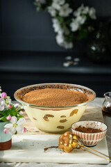 Classic tiramisu dessert in big glass bowl on wooden board on dark blue background.