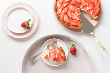 A delicious, fresh tart with pudding cream and strawberries. A piece of grated on a plate. Everything on a white table... - 435213455