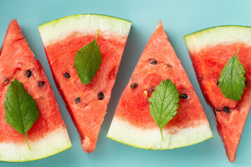 Juicy watermelon triangles, decorated with mint leaves on a turquoise background. A holiday snack for a hot day. - 435213645