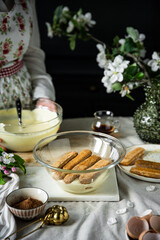 Process of making tiramisu. Layering mascarpone cream and ladyfingers soaked in coffee with alcohol .