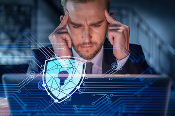 Handsome businessman in suit at workplace working with laptop to defend customer cyber security. Concept of clients information protection and brainstorm. Padlock hologram over office background.