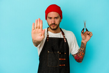 Young tattooed barber man isolated on blue background standing with outstretched hand showing stop sign, preventing you.