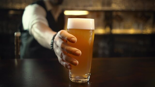 Bartender serving customers in pub, puts pint of beer. Mug of unfiltered beer.