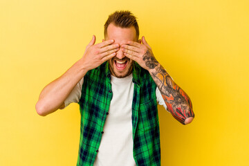 Young tattooed caucasian man isolated on yellow background covers eyes with hands, smiles broadly waiting for a surprise.