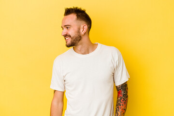 Young tattooed caucasian man isolated on yellow background laughs happily and has fun keeping hands...
