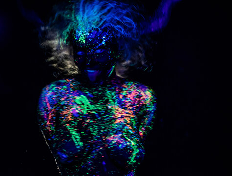 The girl in the image of the devil, contact lenses and horns. Woman paints her tongue in ultraviolet paint. fluorescent powder. Body art glowing in ultraviolet light. Stars in the eyes.