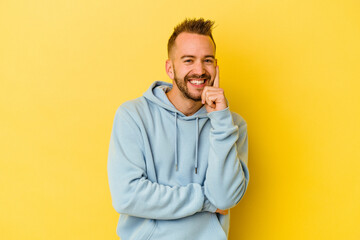 Young tattooed caucasian man isolated on yellow background smiling happy and confident, touching chin with hand.