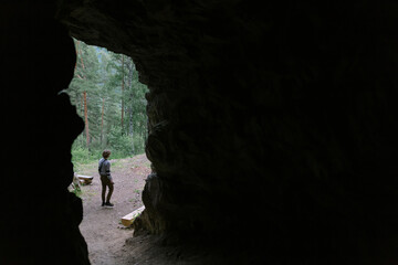 Inside view of the exit from the dark cave: a young man travels in a mountainous forest. Nature of Mountain Altai.