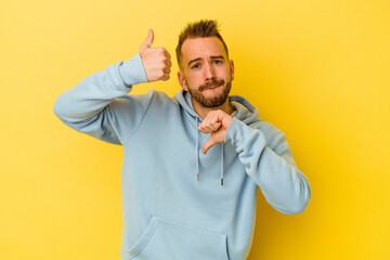 Young tattooed caucasian man isolated on yellow background showing thumbs up and thumbs down, difficult choose concept