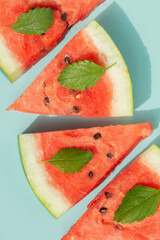 Juicy watermelon triangles, decorated with mint leaves on a turquoise background. A holiday snack for a hot day. - 435216834