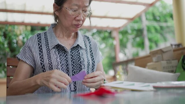 senior asian woman read instruction book to folding paper to make bird origami at home
