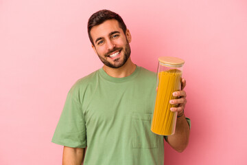 Young caucasian man holding pasta jar isolated on pink background happy, smiling and cheerful.