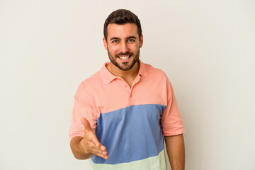 Young caucasian man isolated on white background stretching hand at camera in greeting gesture.