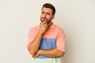 Young caucasian man isolated on white background suspicious, uncertain, examining you.