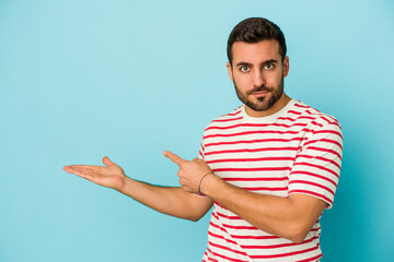 Fototapeta premium Young caucasian man isolated on blue background excited holding a copy space on palm.