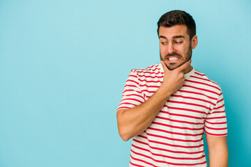 Young caucasian man isolated on blue background touching back of head, thinking and making a choice.