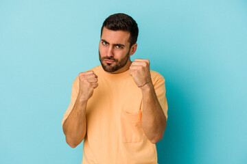 Young caucasian man isolated on blue background showing fist to camera, aggressive facial...