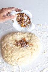Kneading dough with flour and raisins on a white table close-up