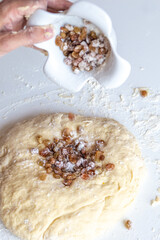 Kneading dough with flour and raisins on a white table close-up
