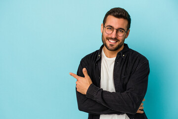 Young caucasian man isolated on blue background smiling cheerfully pointing with forefinger away.