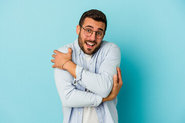Young caucasian man isolated on blue background hugs, smiling carefree and happy.