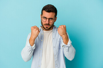 Young caucasian man isolated on blue background showing fist to camera, aggressive facial...