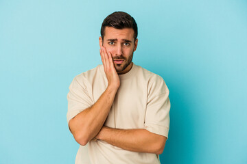 Young caucasian man isolated on blue background blows cheeks, has tired expression. Facial expression concept.