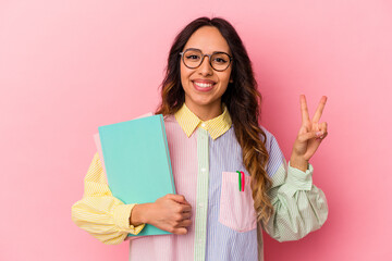 Young student mexican woman isolated on pink background joyful and carefree showing a peace symbol with fingers.