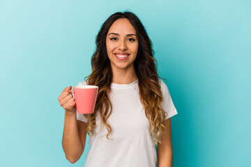 Young mexican woman holding a mug isolated on blue background happy, smiling and cheerful.