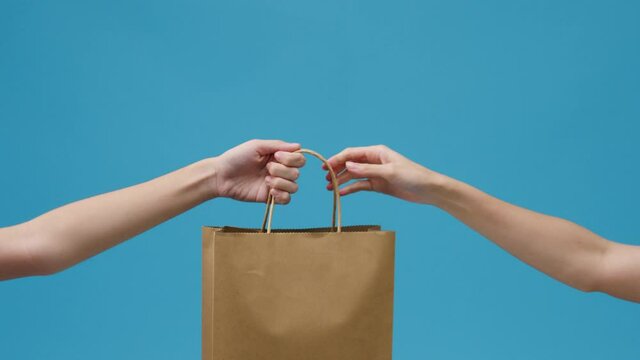 Young woman hand hold brown clear empty blank craft paper bag food for takeaway over blue background. Copy space for place a text for advertisement. Advertising area, mock up promotional content.
